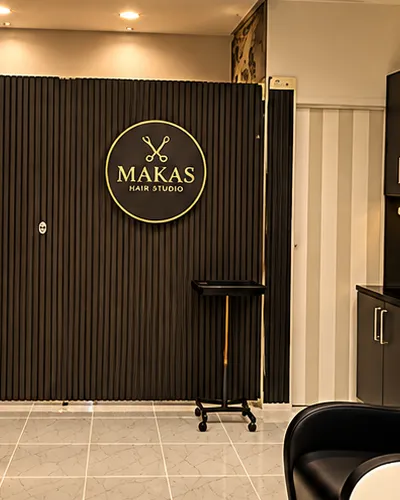 Siyah çıtalı duvarda altın Makas Hair Studio logosu